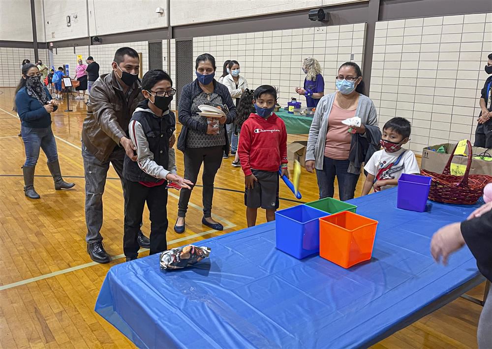 Student playing a toss game while family stands around and watches