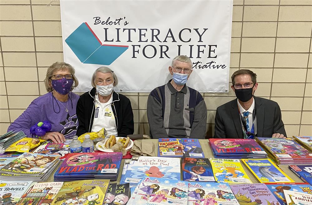 Three adults sitting behind a table of books smiling