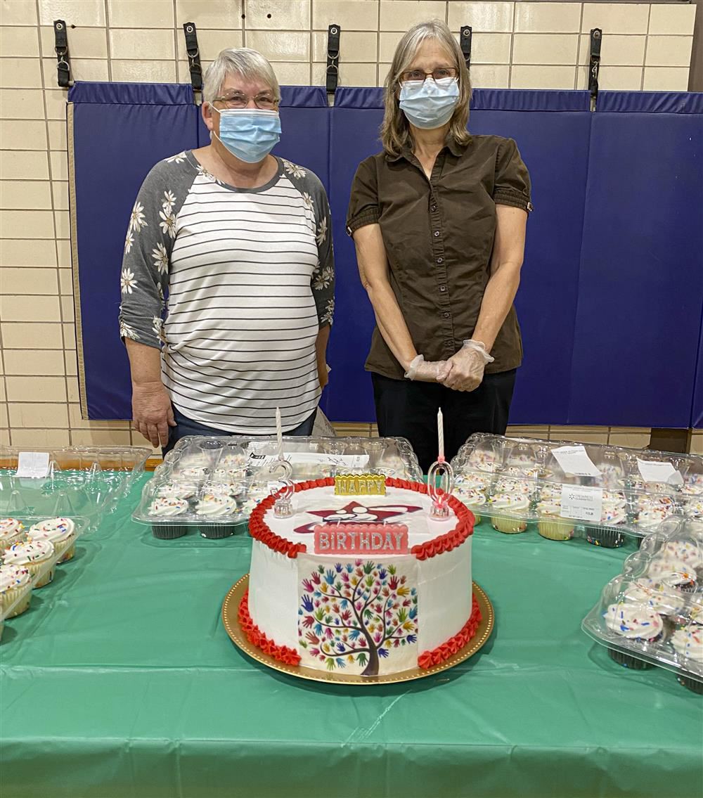 Two adults standing in front of a table with a cake and cupcakes